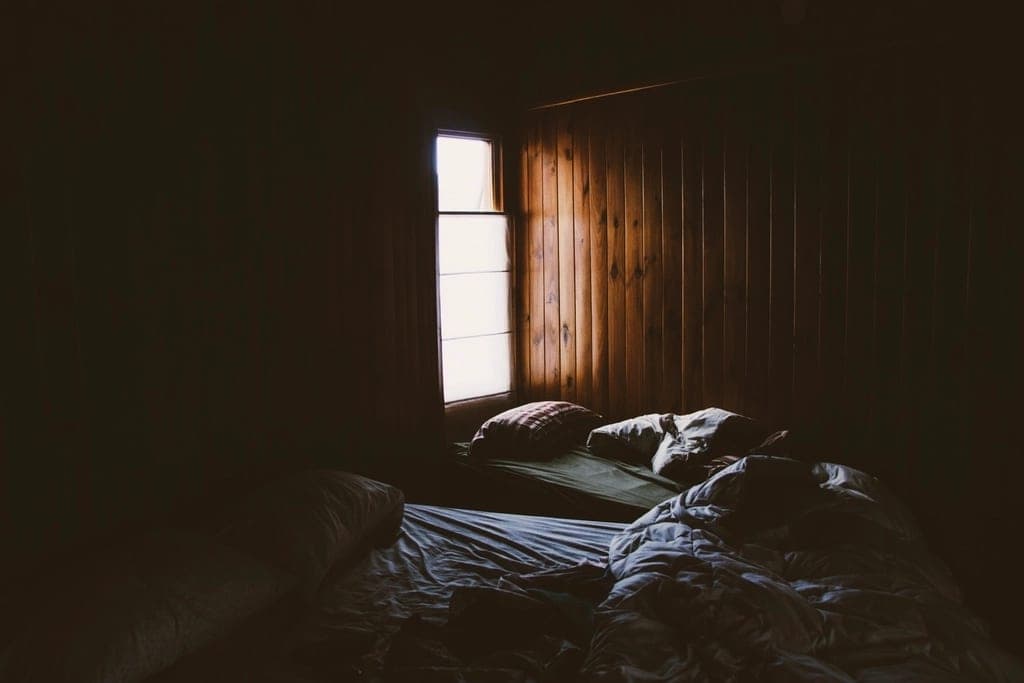 A made bed in a dark bedroom, lit only by a warm bedside lamp