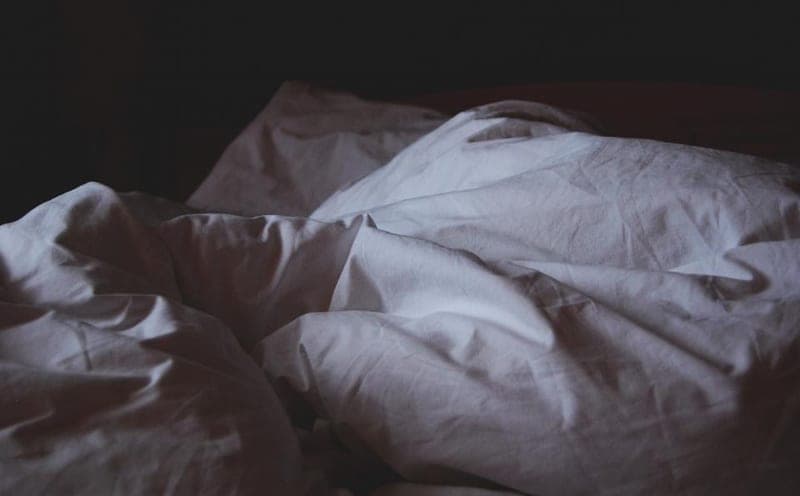 A neatly made bed in a dark, warmly lit bedroom